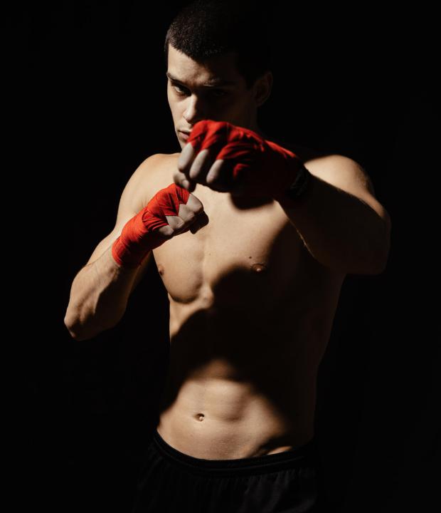 Athletic boxer punching with determination and precaution over black background. Strength, attack and motion concept. Fit caucasian model in movement
